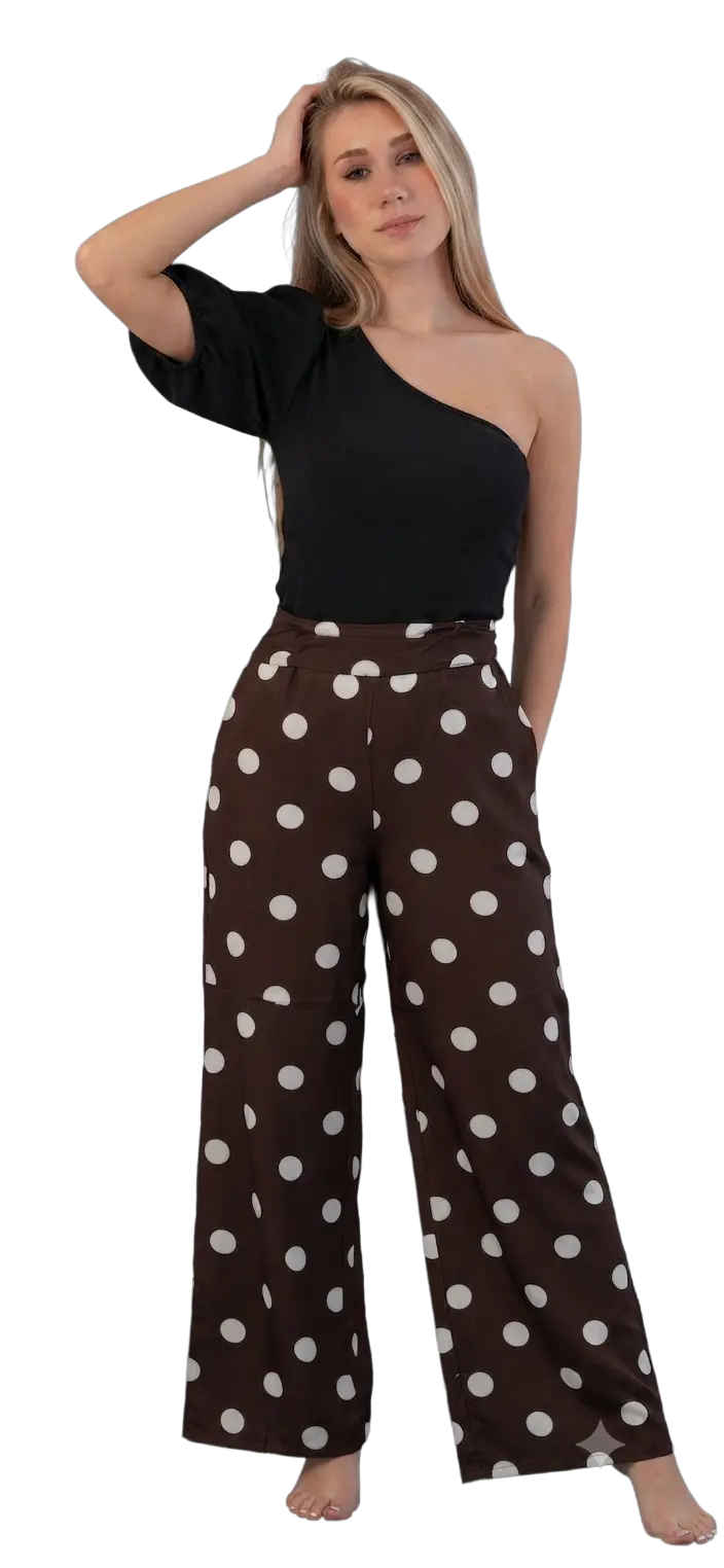 A woman modeling a black one-shoulder top and brown wide-leg pants with white polka dots, posed against a solid white background.