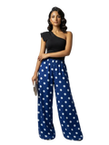 A woman modeling a one-shoulder black top paired with wide-leg blue pants featuring a white polka dot pattern, set against a plain white background.