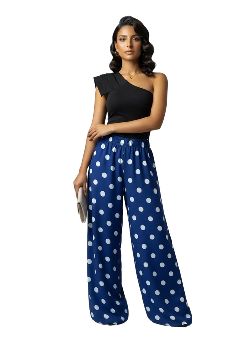 A woman modeling a one-shoulder black top paired with wide-leg blue pants featuring a white polka dot pattern, set against a plain white background.